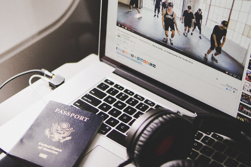 Computer sitting on a airplane tray table with dancers displayed on the computer. USA passport and headphones also resting on computer